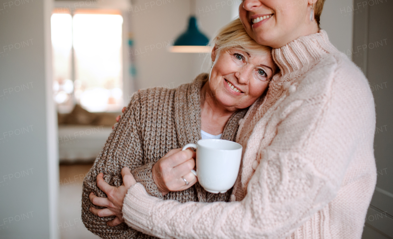 A senior woman with unrecognizable adult daughter at home, hugging.