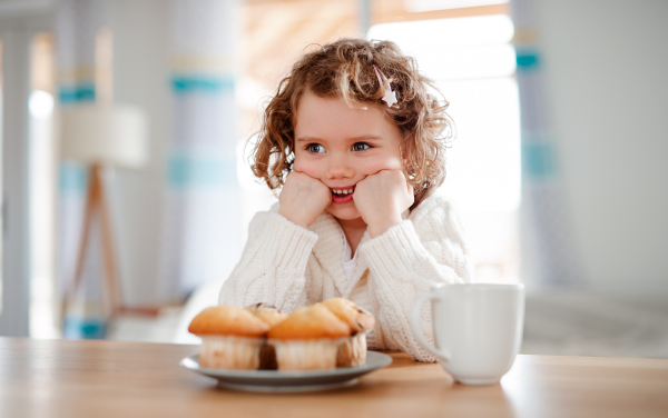 A portrait of happy small girl with muffins sitting at the table at home.