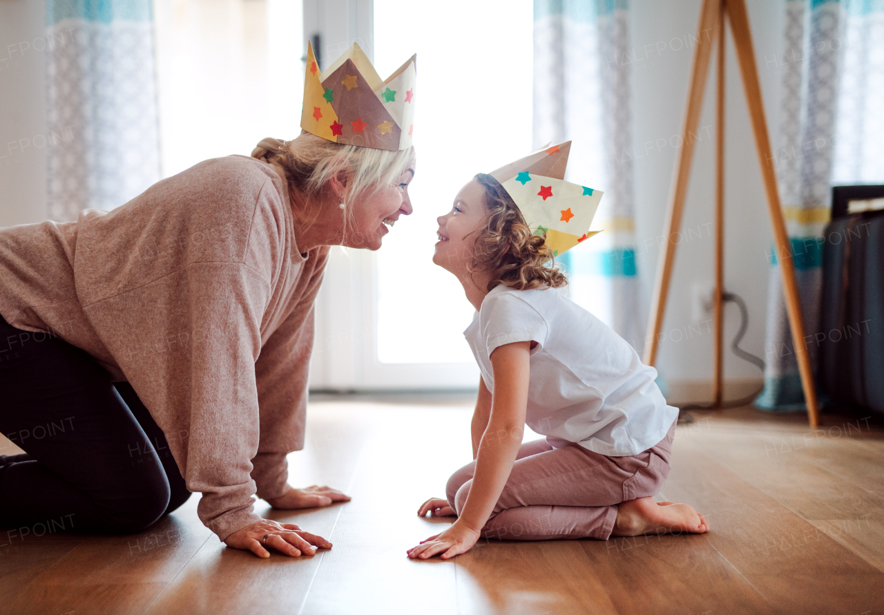 A portrait of small girl and grandmother with paper crown having fun at home.