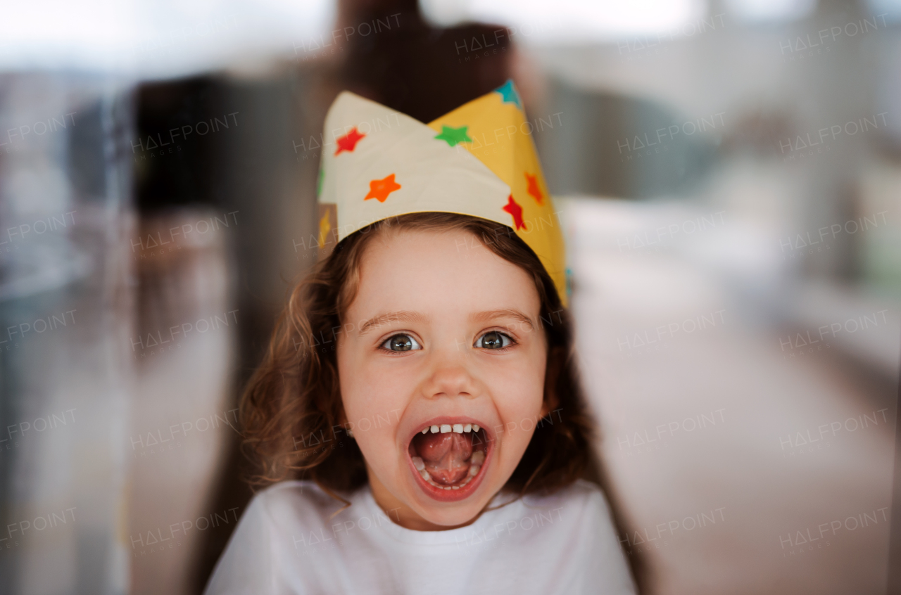 A portrait of small girl with a paper crown at home, looking at camera.