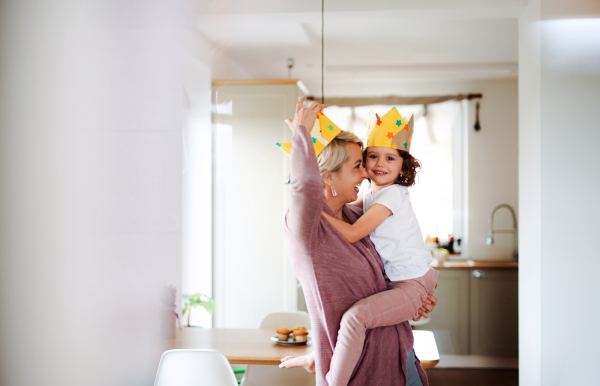 A portrait of small girl and mother with paper crown having fun at home.