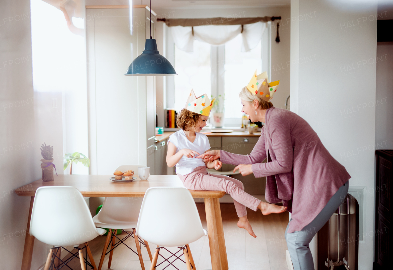 A portrait of small girl and mother with paper crown having fun at home.