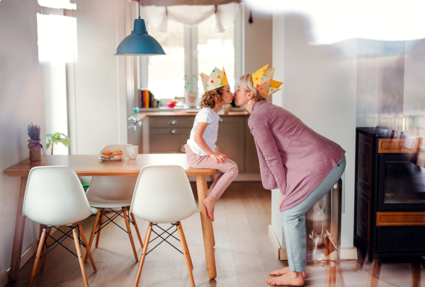 A side view portrait of small girl and mother with paper crown at home, kissing.