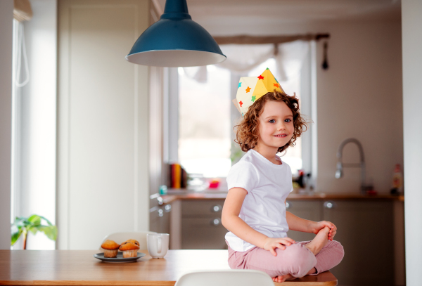 A portrait of small girl with a paper crown at home, looking at camera.