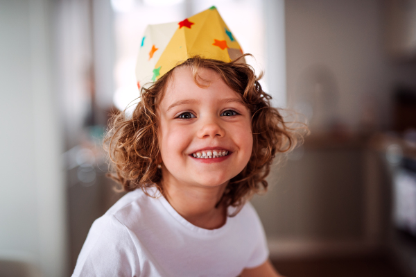 A portrait of small girl with a paper crown at home, looking at camera.