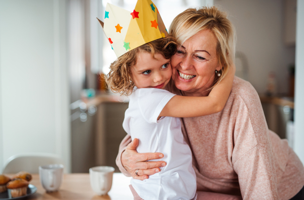 A portrait of small girl and grandmother with paper crown hugging at home.