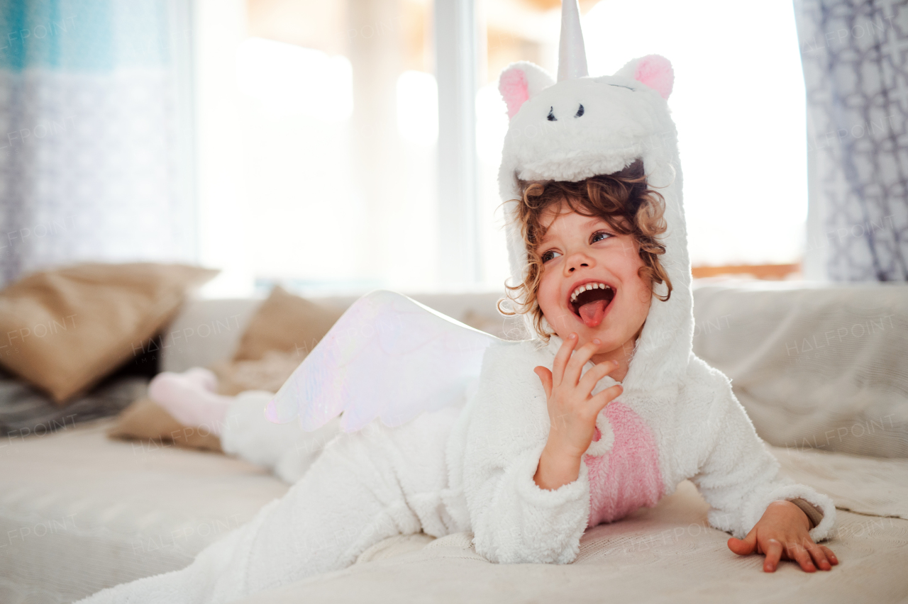 A portrait of happy small girl in unicorn mask lying on sofa at home.