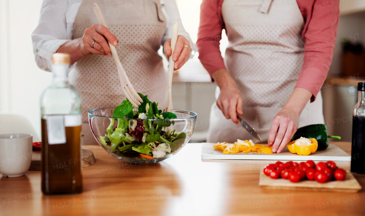 A midsection of unrecognizable women at home, preparing vegetable salad.