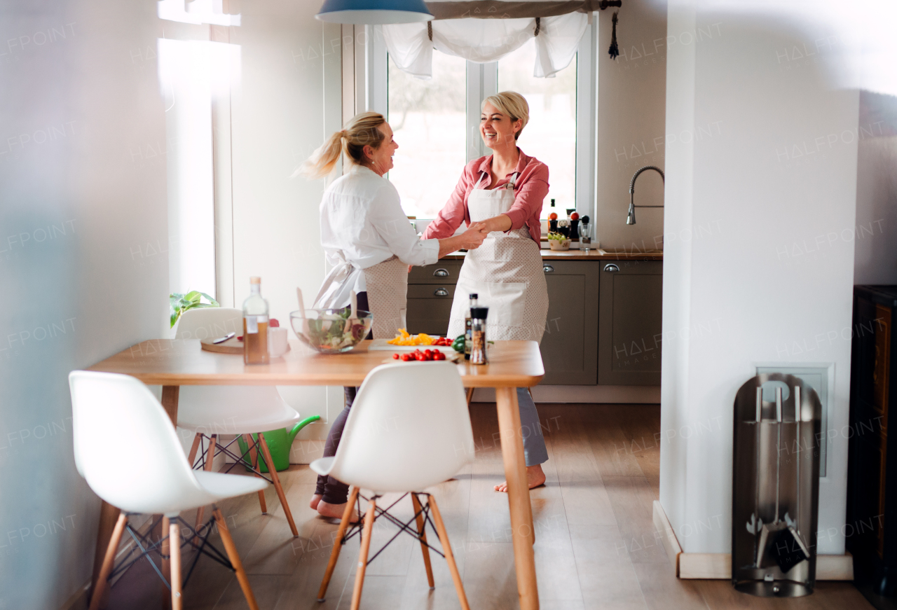 A young woman dancing with senior mother at home, having fun when cooking.