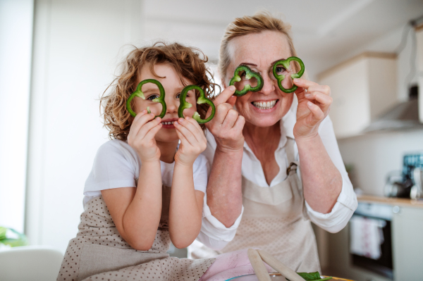 A portrait of happy small girl with grandmother preparing vegetable salad at home, having fun.