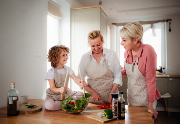 A portrait of small girl with mother and grandmother at home, preparing vegetable salad.