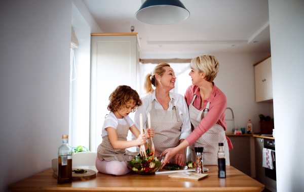 A portrait of small girl with mother and grandmother at home, preparing vegetable salad.