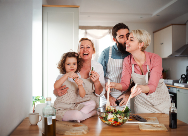 A portrait of small girl with parents and grandmother at home, preparing vegetable salad.