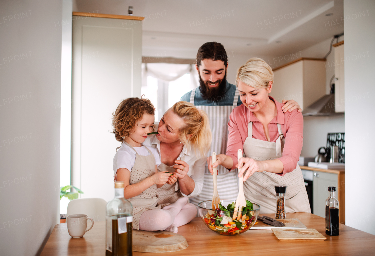 A portrait of small girl with parents and grandmother at home, preparing vegetable salad.