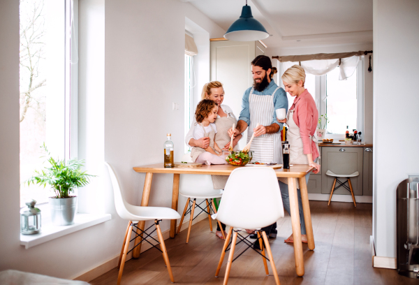 A portrait of small girl with parents and grandmother at home, preparing vegetable salad.