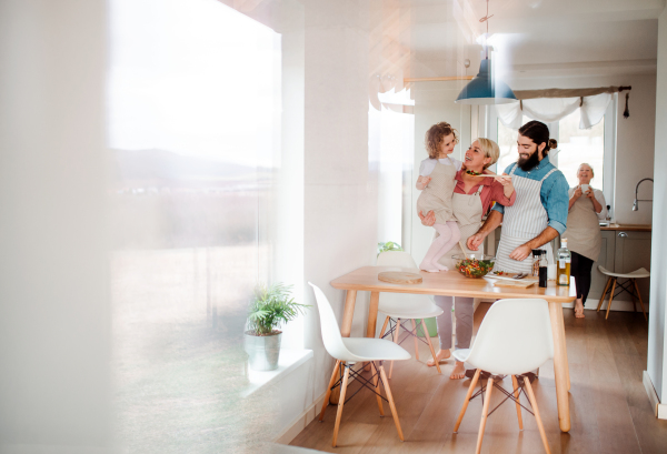 A portrait of small girl with parents and grandmother at home, preparing vegetable salad.