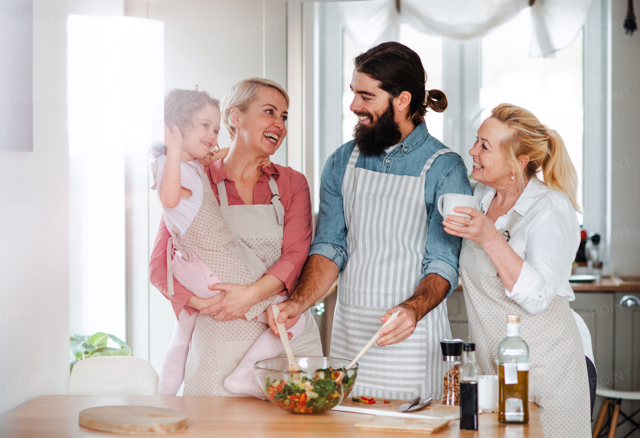 A portrait of small girl with parents and grandmother at home, preparing vegetable salad.