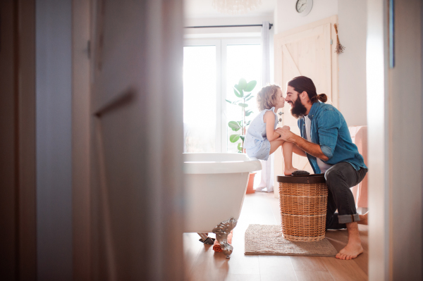 A happy small girl with young father in bathroom at home, having fun.