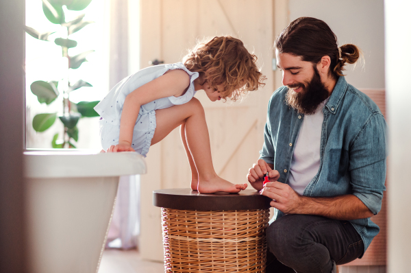 A young father painting small daughter's nails in a bathroom at home.