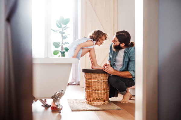 A young father painting small daughter's nails in a bathroom at home.