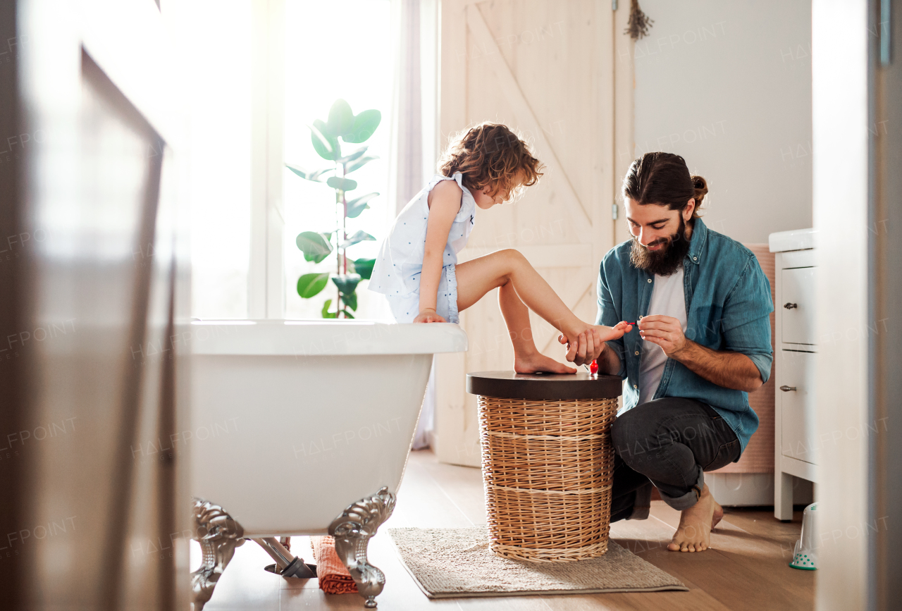 A young father painting small daughter's nails in a bathroom at home.