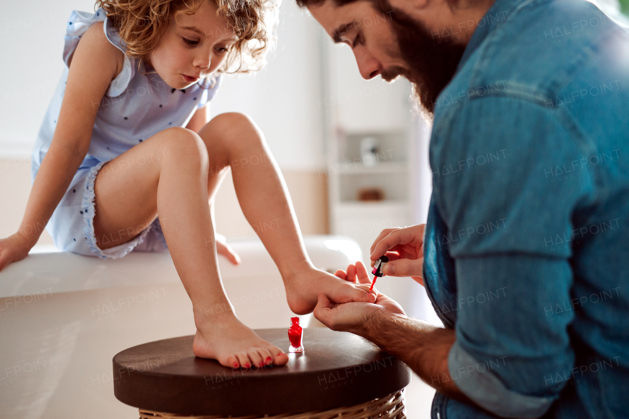 A young father painting small daughter's nails in a bathroom at home.