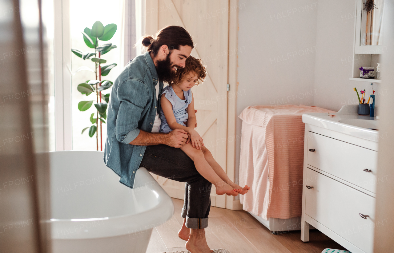 A small girl with young father in bathroom at home, looking at painted nails on feet.