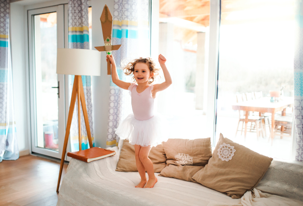 A portrait of small girl with a princess dress at home, holding a toy sword and jumping.