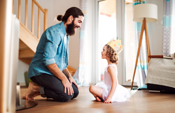 A side view of small girl with a princess crown and young father at home, playing.