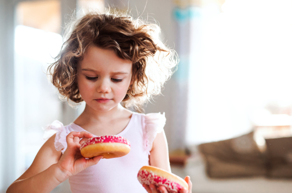 A portrait of small girl with two doughnuts at home..