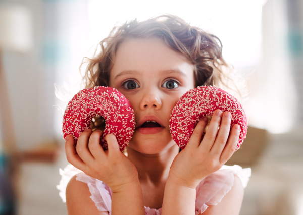 A portrait of small girl with two doughnuts at home, looking at camera.