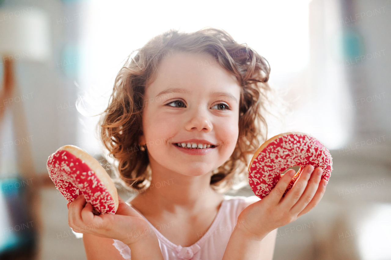 A portrait of small girl with two doughnuts at home, having fun.