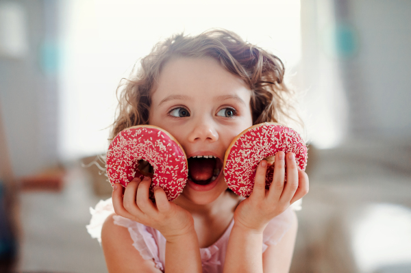 A portrait of small girl with two doughnuts at home, looking at camera.