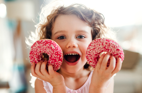 A portrait of small girl with two doughnuts at home, looking at camera.