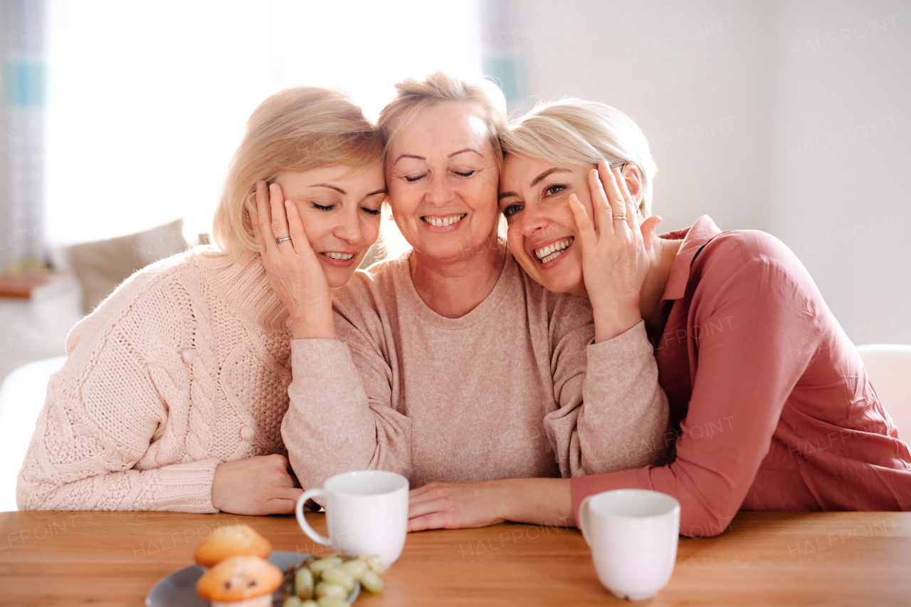 A happy senior mother with two adult daughters sitting at the table at home.