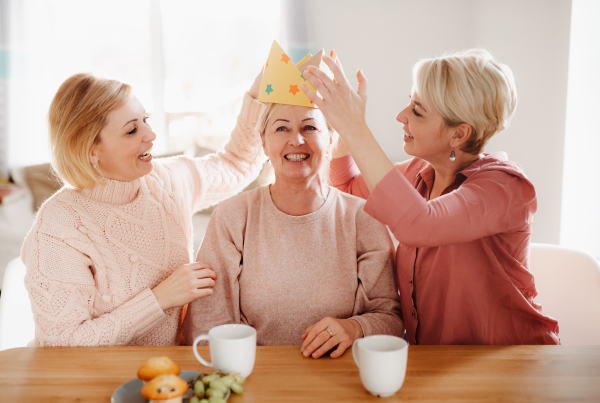 A happy senior mother with two adult daughters sitting at the table at home, having fun.