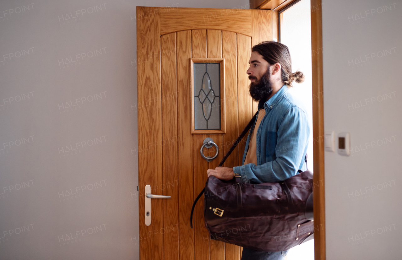 A young hipster man with bag entering front door when coming back home.