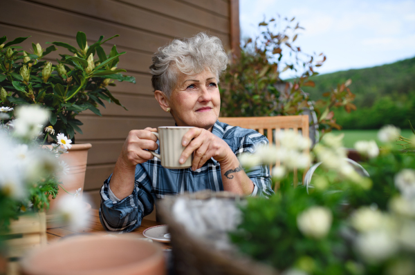 Portrait of senior woman with coffee sitting on terrace in summer, resting.