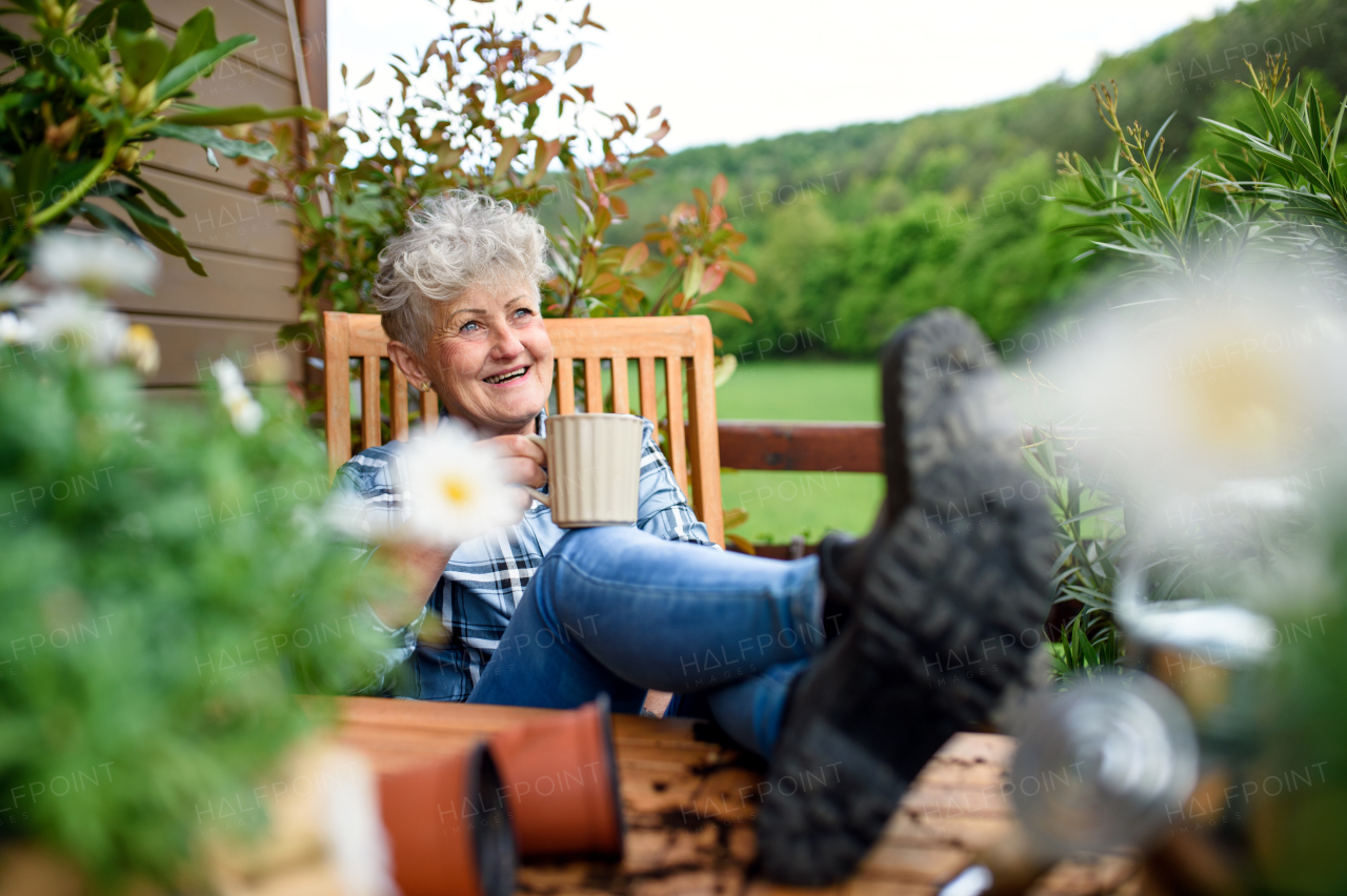 Portrait of senior woman with coffee sitting on terrace in summer, resting.