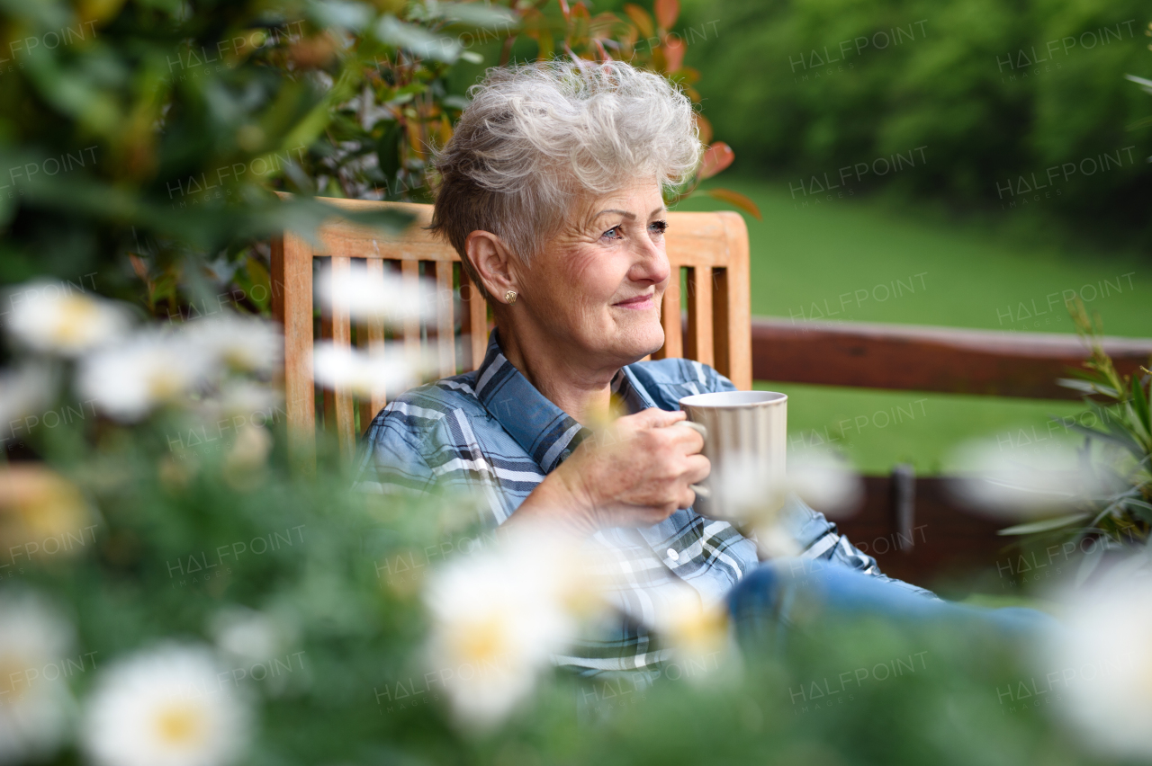 Portrait of senior woman with coffee sitting on terrace in summer, resting.