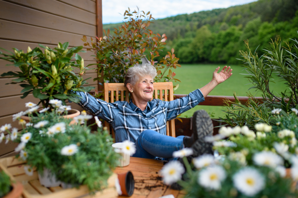 Cheerful senior grandmother gardening on balcony in summer, resting.