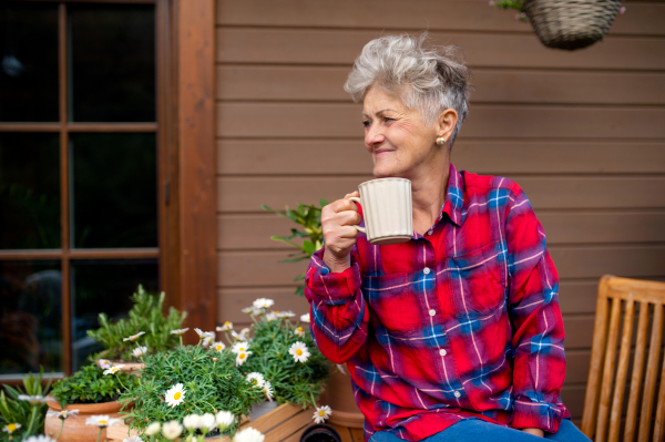 Portrait of senior woman with coffee sitting on terrace in summer, resting.