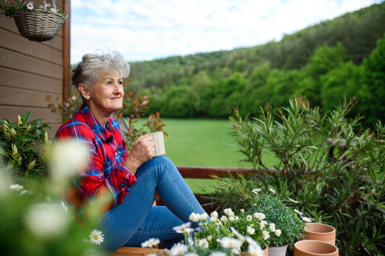 Portrait of senior woman with coffee sitting on terrace in summer, resting.