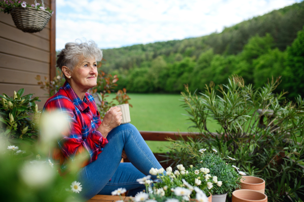 Portrait of senior woman with coffee sitting on terrace in summer, resting.