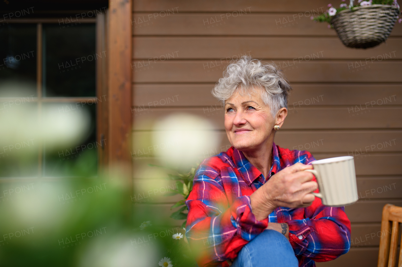 Portrait of senior woman with coffee sitting on terrace in summer, resting.