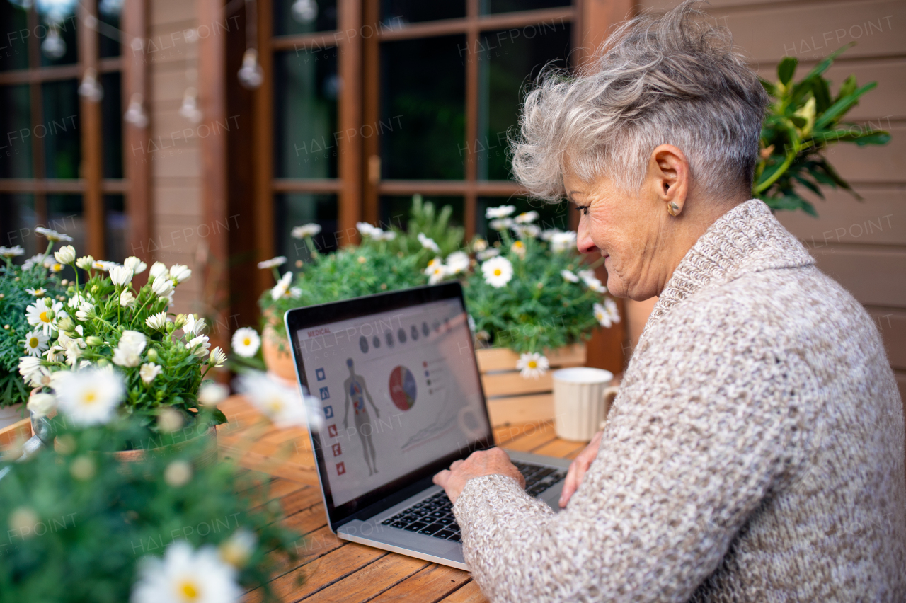 Portrait of senior woman with laptop and coffee sitting on terrace in summer, resting.