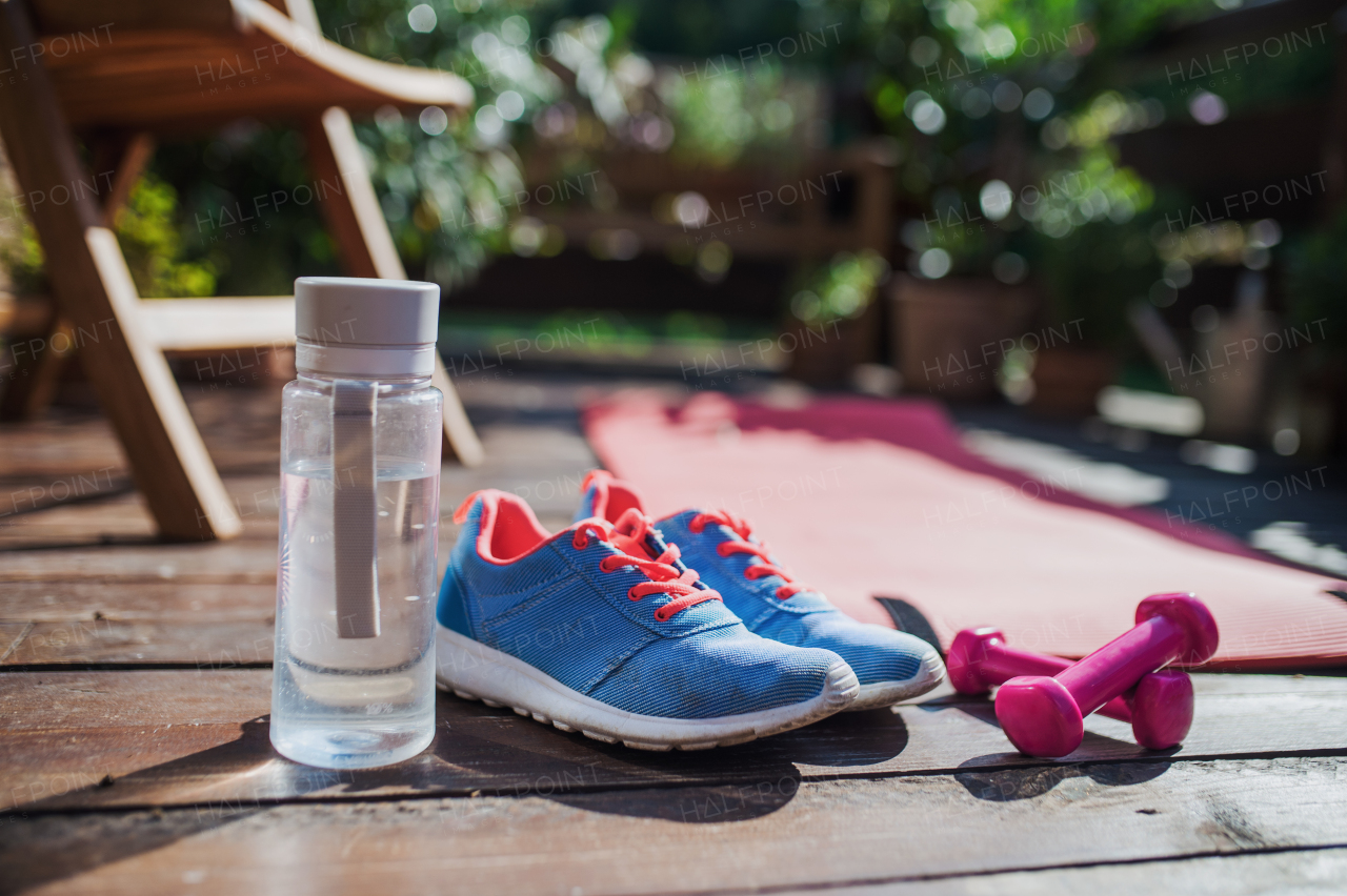 Water bottle, blue trainers and dumbbells outdoors on a terrace in summer.