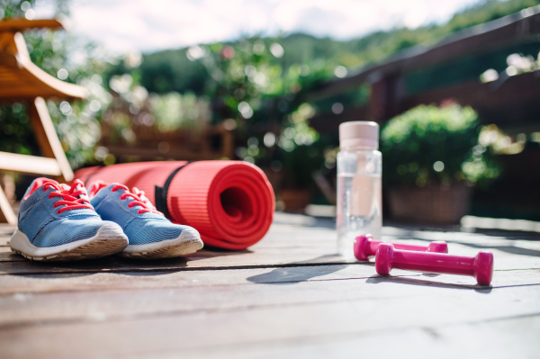 Water bottle, blue trainers and dumbbells outdoors on a terrace in summer.