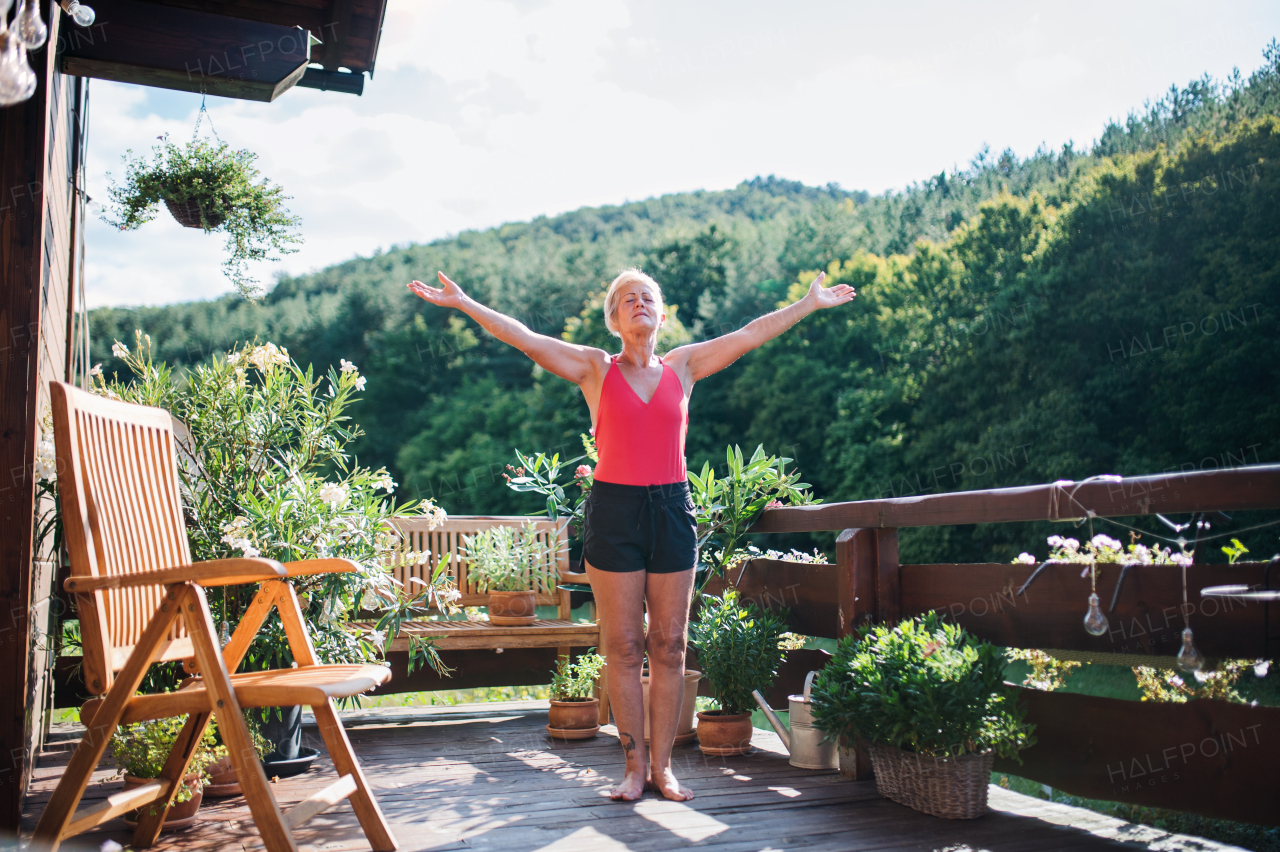 A senior woman standing outdoors on a terrace in summer, doing exercise. Copy space.