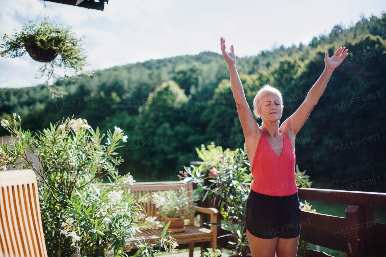 A senior woman standing outdoors on a terrace in summer, doing exercise. Copy space.